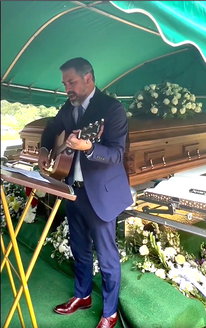 貝克議員在靈柩前彈吉他唱詩歌送女兒女婿最後一程。（臉書影片截圖）